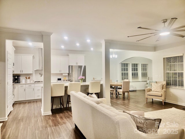 living room featuring ornamental molding, ceiling fan with notable chandelier, and light hardwood / wood-style flooring