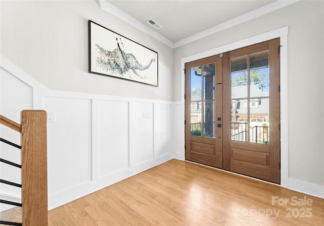 entryway featuring stairway, wood finished floors, ornamental molding, french doors, and a decorative wall