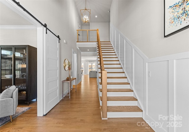 foyer with stairway, a barn door, an inviting chandelier, light wood-style floors, and a decorative wall