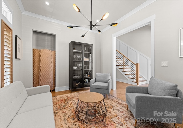 living area featuring wood finished floors, baseboards, an inviting chandelier, ornamental molding, and stairs