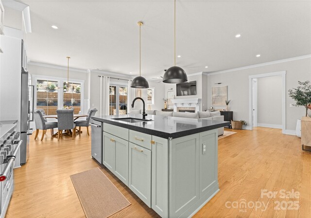 kitchen with light wood finished floors, a fireplace, a kitchen island with sink, a sink, and hanging light fixtures