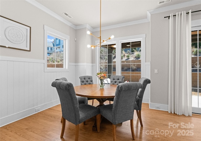 dining room featuring visible vents, light wood-style flooring, ornamental molding, and a wainscoted wall