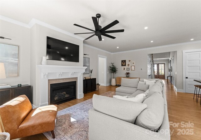 living room featuring crown molding, baseboards, recessed lighting, light wood-style flooring, and a glass covered fireplace