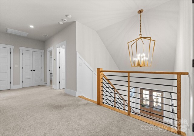 corridor with an upstairs landing, carpet flooring, baseboards, and an inviting chandelier