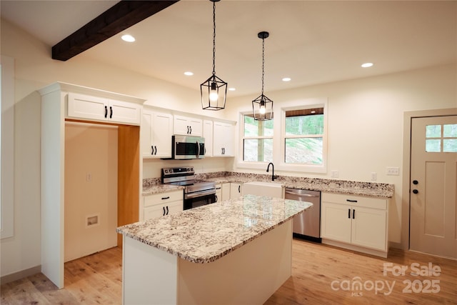 kitchen featuring a center island, white cabinetry, light stone counters, appliances with stainless steel finishes, and hanging light fixtures