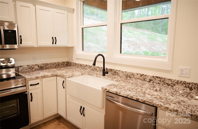 kitchen featuring light wood-style floors, white cabinetry, light stone counters, a sink, and stainless steel appliances