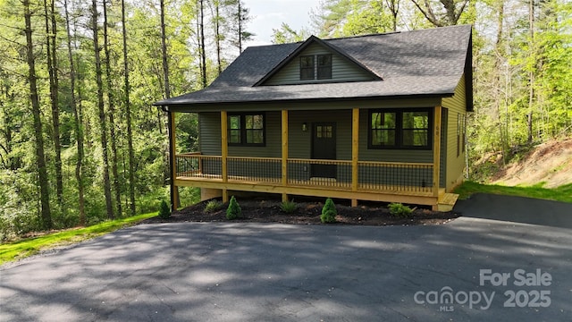 view of front facade with a view of trees, a shingled roof, and a porch