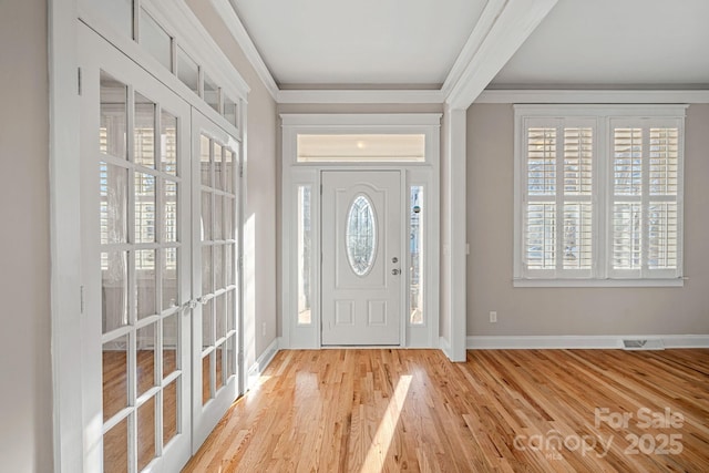 foyer entrance featuring ornamental molding, french doors, and light wood-type flooring