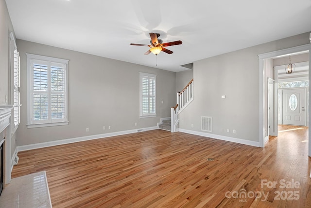 unfurnished living room featuring a wealth of natural light, ceiling fan with notable chandelier, and light wood-type flooring