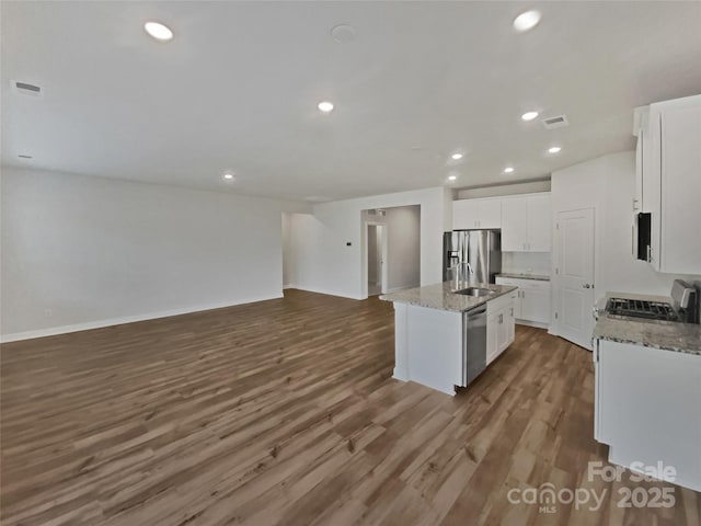 kitchen with appliances with stainless steel finishes, dark wood-type flooring, a center island with sink, and white cabinets