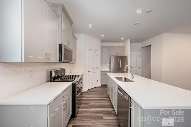 kitchen featuring gray cabinets, dark hardwood / wood-style floors, sink, stainless steel appliances, and a center island with sink