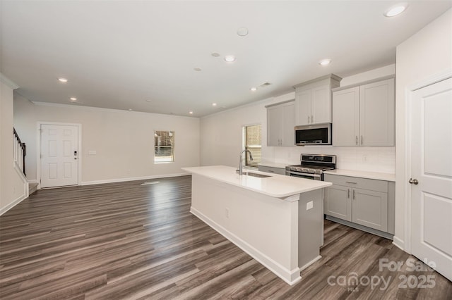 kitchen with sink, appliances with stainless steel finishes, dark hardwood / wood-style flooring, gray cabinets, and an island with sink