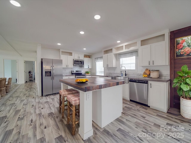 kitchen featuring sink, wooden counters, appliances with stainless steel finishes, white cabinetry, and a center island