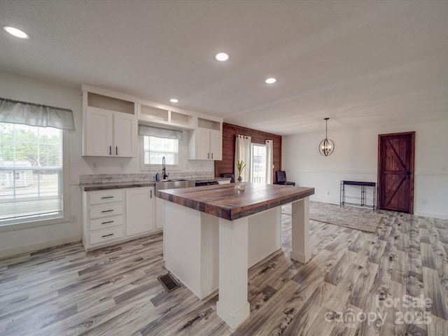 kitchen with butcher block counters, decorative light fixtures, white cabinets, and a kitchen island