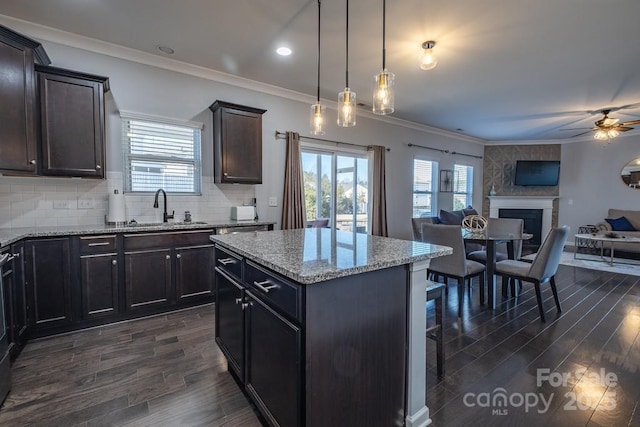 kitchen with sink, hanging light fixtures, a center island, light stone countertops, and a large fireplace