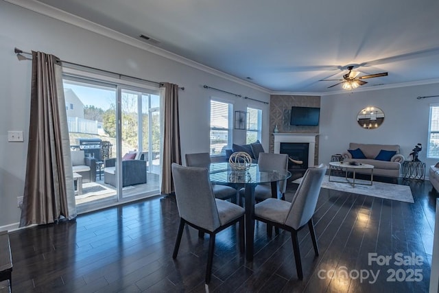 dining area featuring a fireplace, crown molding, dark wood-type flooring, and ceiling fan