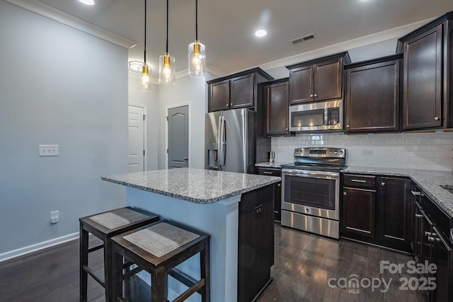 kitchen with tasteful backsplash, a center island, hanging light fixtures, stainless steel appliances, and light stone countertops