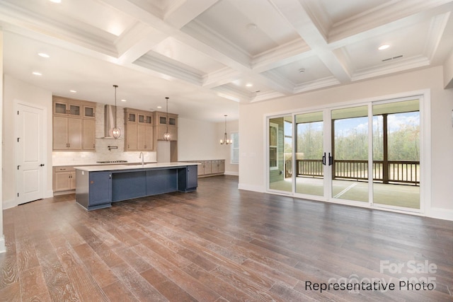 kitchen with dark wood-type flooring, wall chimney exhaust hood, beamed ceiling, pendant lighting, and a kitchen island with sink