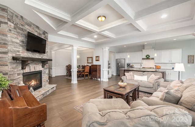 living room with a stone fireplace, dark wood-type flooring, beamed ceiling, and ornate columns