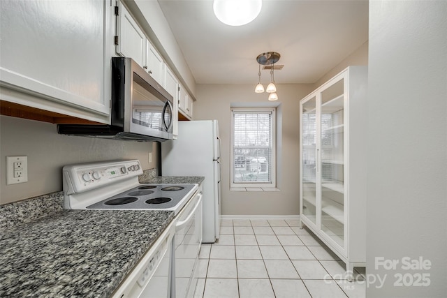 kitchen with hanging light fixtures, light tile patterned floors, white appliances, dark stone counters, and white cabinets