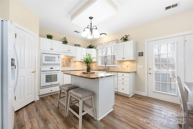 kitchen featuring white cabinetry, a kitchen island, white appliances, and decorative light fixtures