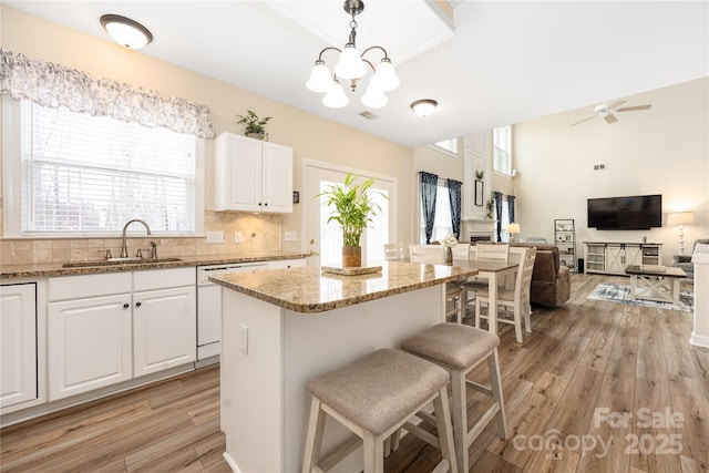 kitchen with sink, hanging light fixtures, a kitchen island, light stone countertops, and white cabinets