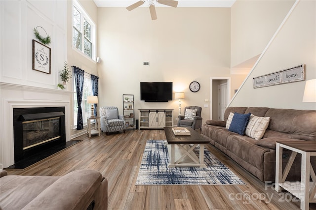 living room with a towering ceiling, wood-type flooring, ceiling fan, and plenty of natural light