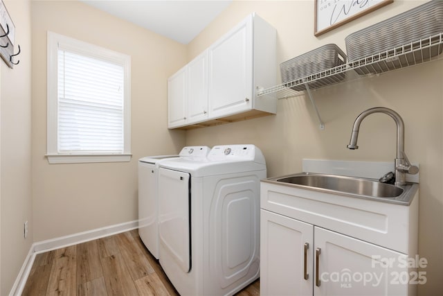 clothes washing area with cabinets, washing machine and dryer, sink, and light hardwood / wood-style flooring