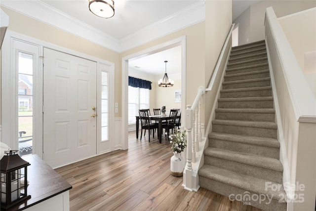 foyer entrance featuring hardwood / wood-style flooring, ornamental molding, and a notable chandelier