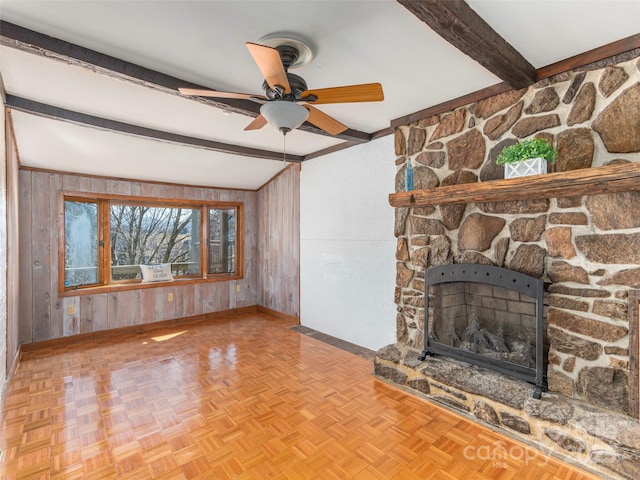 unfurnished living room with lofted ceiling with beams, light parquet flooring, a stone fireplace, and wooden walls