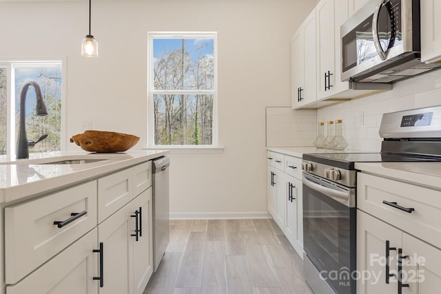 kitchen with decorative light fixtures, sink, white cabinets, backsplash, and stainless steel appliances