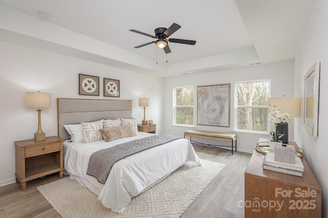 bedroom with a raised ceiling, ceiling fan, and light wood-type flooring