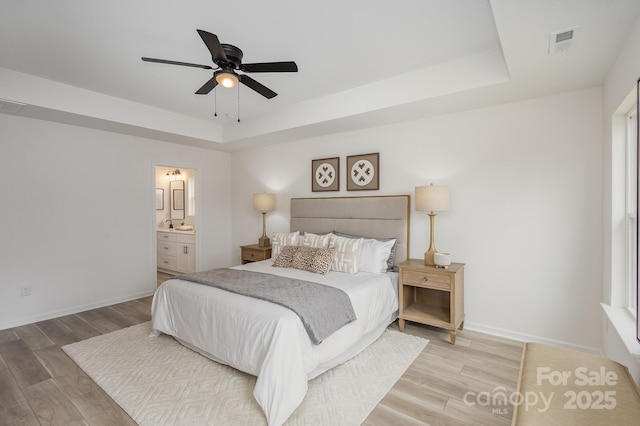 bedroom featuring connected bathroom, hardwood / wood-style floors, and a tray ceiling