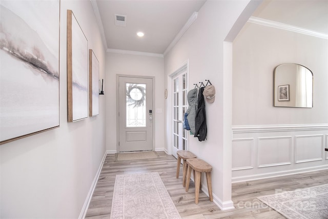 foyer with light wood-style flooring, visible vents, arched walkways, and crown molding