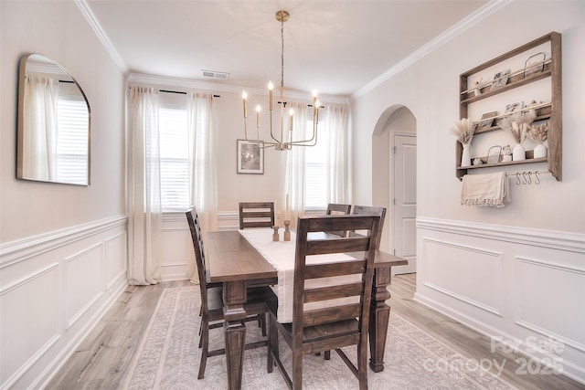 dining room with light wood finished floors, visible vents, arched walkways, wainscoting, and ornamental molding