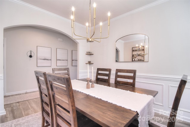 dining room featuring arched walkways, a wainscoted wall, crown molding, a decorative wall, and wood finished floors