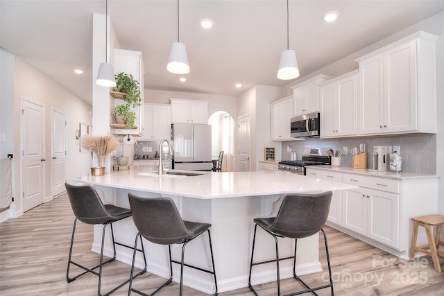 kitchen featuring arched walkways, stainless steel appliances, backsplash, a sink, and a kitchen bar