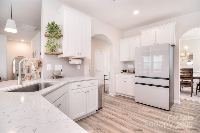 kitchen with light wood-type flooring, freestanding refrigerator, white cabinets, and a sink