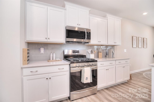 kitchen featuring stainless steel appliances, white cabinets, light wood-style floors, light countertops, and tasteful backsplash