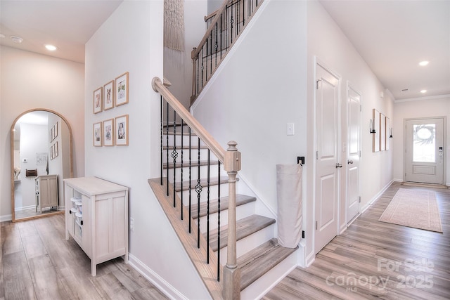 entrance foyer with light wood finished floors, baseboards, arched walkways, stairs, and recessed lighting