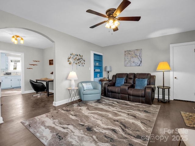 living room with arched walkways, dark wood-style flooring, ceiling fan, and baseboards