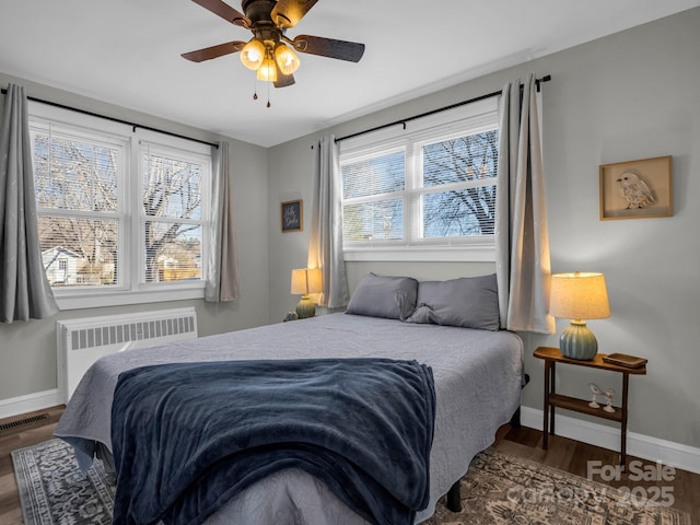 bedroom with a ceiling fan, baseboards, visible vents, radiator, and dark wood finished floors