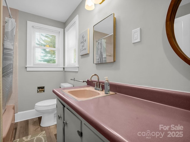 bathroom with toilet, wood finished floors, vanity, baseboards, and shower / bath combination with curtain