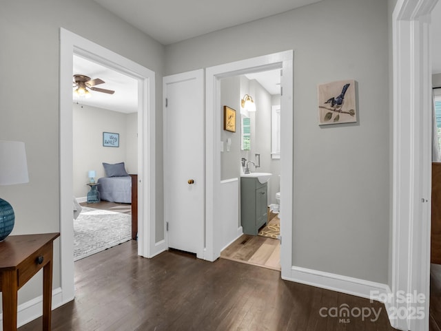 corridor with dark wood-style floors, baseboards, and a sink