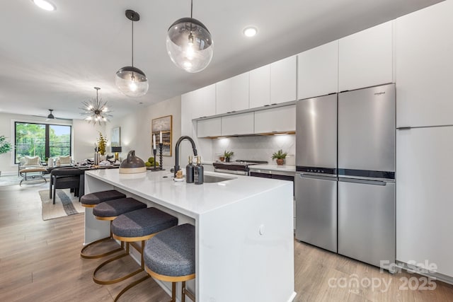 kitchen with pendant lighting, stainless steel refrigerator, sink, white cabinets, and a center island with sink