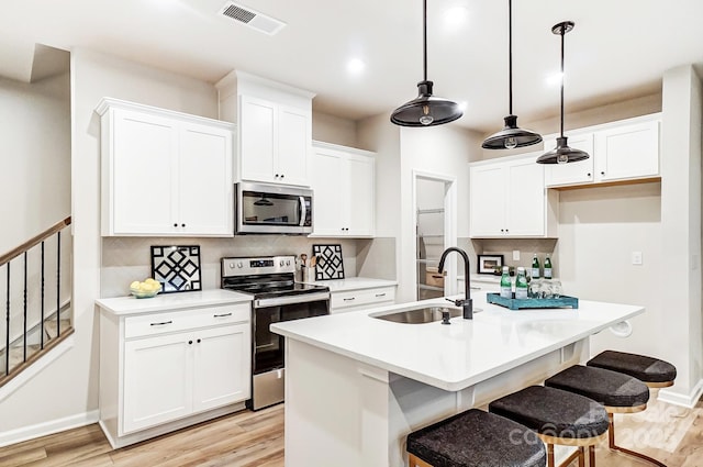 kitchen featuring pendant lighting, sink, appliances with stainless steel finishes, white cabinetry, and a kitchen island with sink