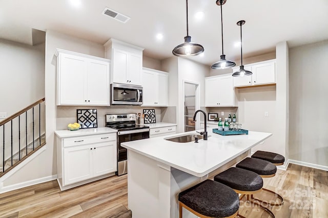 kitchen with decorative light fixtures, an island with sink, sink, white cabinets, and stainless steel appliances