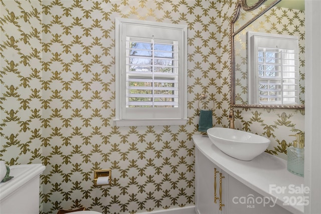 half bathroom with toilet, wallpapered walls, and vanity