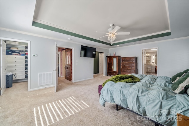 bedroom featuring baseboards, visible vents, a walk in closet, crown molding, and a tray ceiling