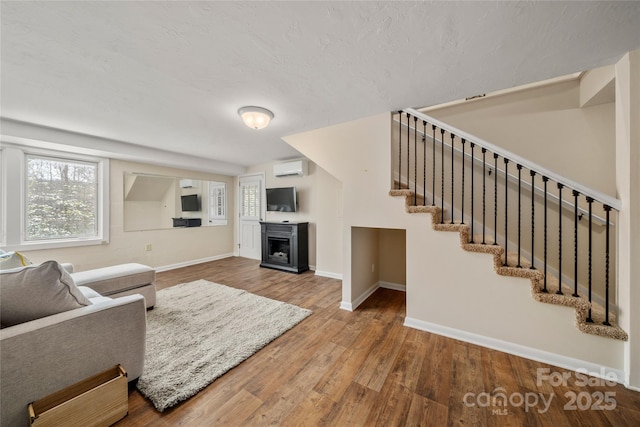 living room featuring a fireplace, an AC wall unit, baseboards, wood finished floors, and stairway